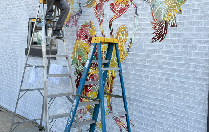 Richie Morales on a ladder next to a mural in progress