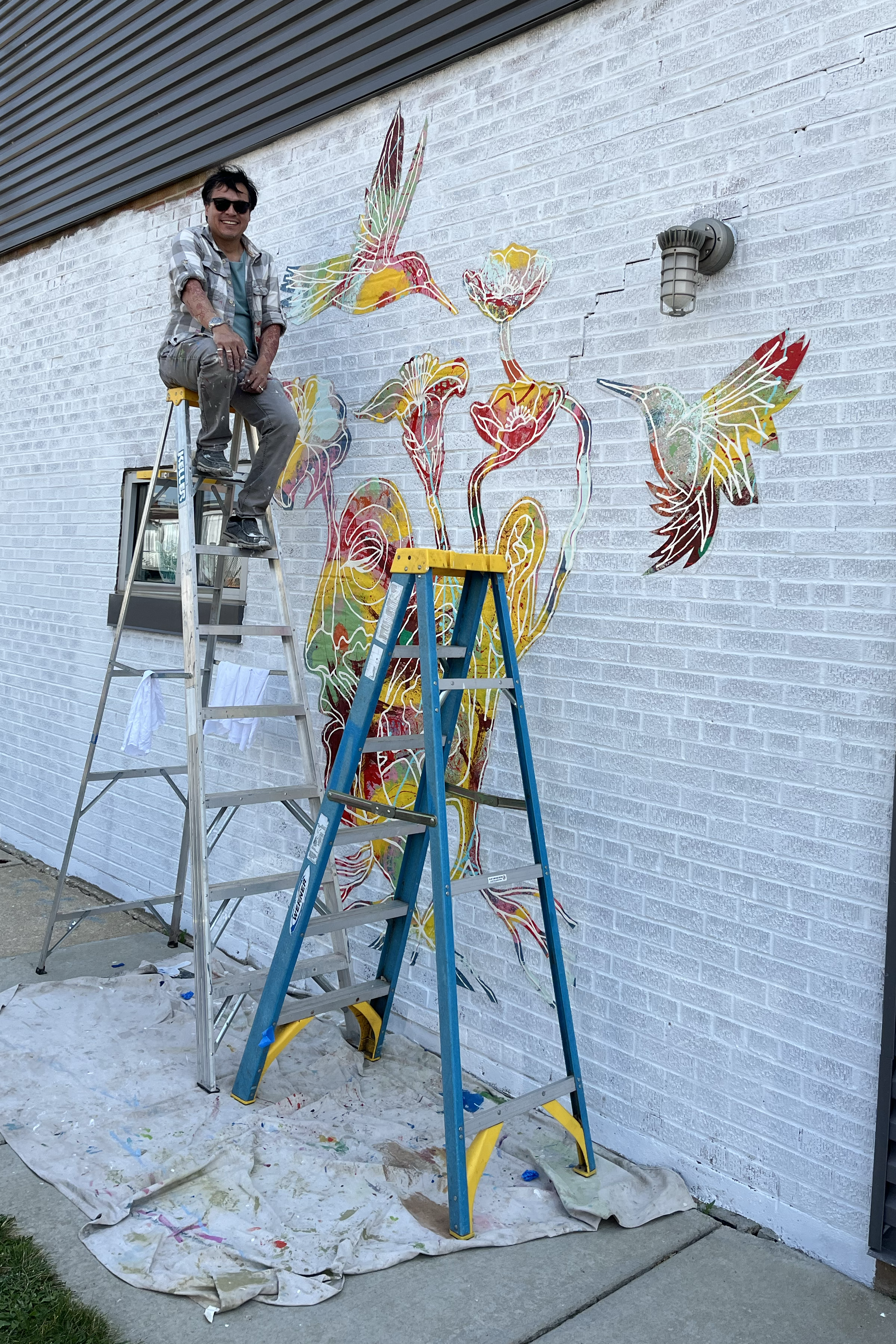 Richie Morales on a ladder next to a mural in progress